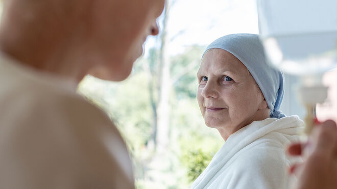 Ältere Frau mit Kopftuch empfängt eine Chemotherapie und blickt auf die Pflegerin, welche den Tropf einstellt | GettyImages / KatarzynaBialasiewicz
